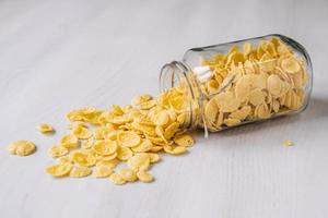 Copos de maíz en un frasco de vidrio sobre mesa de madera blanca foto