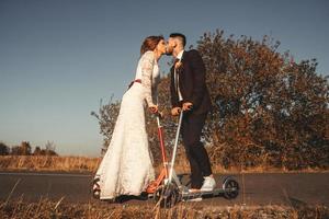 Kissing wedding couple riding a on scooters along road photo