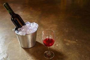 botella de vino tinto en un cubo de hielo y una copa de vino tinto foto