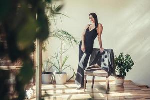 Woman dressed in black clothes standing near armchair in loft style interior photo