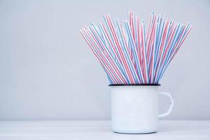 Beber pajitas de plástico en taza de metal blanco sobre un fondo gris foto