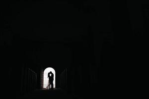 Silhouette of loving couple hugging while standing in doorway on black background photo