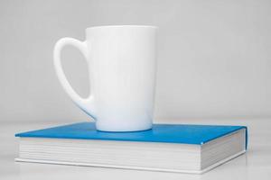 White ceramic cup and book on white table photo