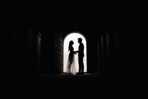 Silhouette of loving couple hugging while standing in doorway on black background photo