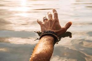 Man touches the water with his hand at sunset photo