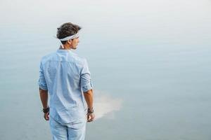 Hombre vestido con ropa ligera mira el reflejo del agua del cielo azul foto