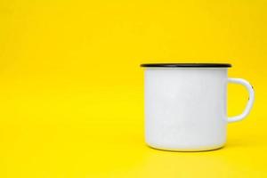 Taza de metal blanco esmaltado con línea negra en el borde sobre fondo amarillo foto