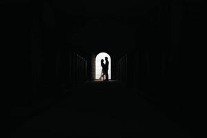 Silhouette of loving couple hugging while standing in doorway on black background photo