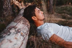 Man lies on grass, resting his head on a log in middle of forest relaxing photo
