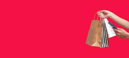 Woman shopping online from a mobile phone. Female hands with packages isolated on red background, copy space. Banner photo