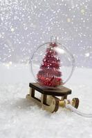 en la nieve - un trineo con una bola de Navidad dentro de un árbol de Navidad sobre un fondo de primer plano de luces bokeh. foto vertical