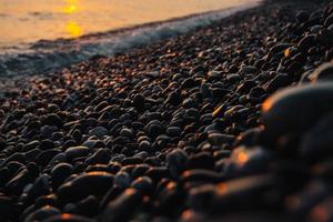 Small stones by the sea with bokeh effect. Blurred decorative background, place for text. Summer wallpaper, sunny sunset light photo
