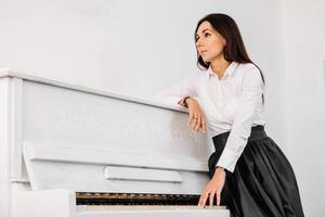 Beautiful woman dressed in white shirt playing on white piano. Place for text or advertising