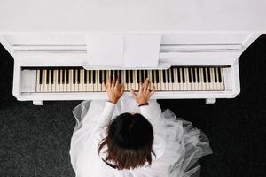 Beautiful woman dressed in white dress playing on white piano. Top view photo