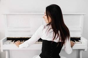 Beautiful woman dressed in white dress playing on white piano
