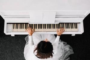 Beautiful woman dressed in white dress playing on white piano. Top view