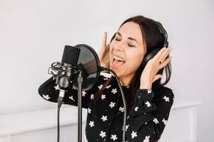 hermosa mujer en auriculares canta una canción cerca de un micrófono en un estudio de grabación. lugar para texto o publicidad foto