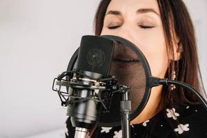 Retrato de mujer hermosa canta una canción cerca de un micrófono en un estudio de grabación. cara de primer plano foto