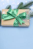 Merry Christmas and Happy New Year. Gift with a green ribbon with polka dots and ornaments on a blue background with lights. Holiday card copy space close up. Vertical photo