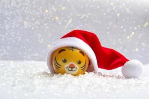 The symbol of the new year is a tiger in a Santa hat on the snow against a background of bokeh lights. Close up of new year photo