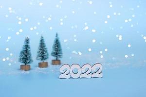 Merry Christmas and Happy New Year. Wooden numbers 2022 against the backdrop of lights and Christmas trees on a blue background. Holiday card copy space close up photo