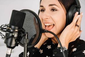 Beautiful woman in headphones sings a song near a microphone in a recording studio. Place for text or advertising photo