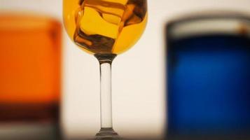 Closeup photo of drink in a glass with ice cubes on a bokeh blur background of colored drink glasses