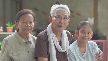 portret van gelukkige bejaarde grootouders die samen met kleindochter thuis zitten. video