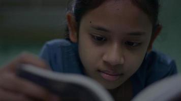 close-up menina bonita lendo um livro e virando as páginas enquanto estava deitado na cama à noite. video