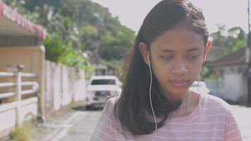 Chica con auriculares caminando por la calle en zona residencial video