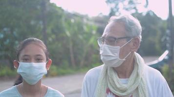 jovencita con su abuelo con máscaras faciales, caminando juntos en la aldea rural.