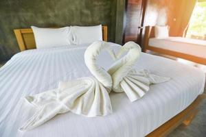Toalla de baño blanca limpia en la decoración de la cama interior del dormitorio - Toalla blanca en la cama en la habitación para el cliente del hotel foto