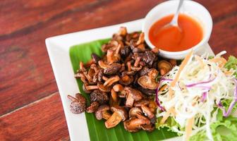 Delicious fried mushrooms in plate on wooden table, top view - cooked shiitake mushrooms fried with tomato sauce and vegetables photo