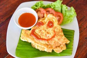 Omelet roll with sliced tomatoes salad lettuce vegetable on white plate - eggs omelette breakfast and tomatoes sauce on top photo