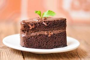 Pastel de chocolate delicioso postre servido en la mesa - rebanada de pastel en un plato blanco con cobertura de chocolate y hojas de menta foto