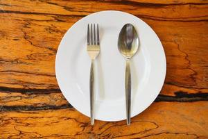 Empty plate with spoon fork on food table wooden background - empty dinner plate dish , top view photo