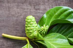 Fruta de noni sobre fondo de madera fresca hoja de noni madura y cruda gran morinda noni o morinda citrifolia foto