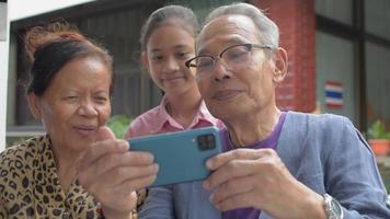 Großeltern und Enkelin chatten zu Hause auf dem Smartphone.