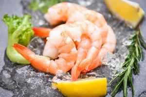 Boiled shrimps prawns on ice frozen at the seafood restaurant - fresh shrimp on dark plate with lemon rosemary ingredients herb and spices for cooking seafood photo