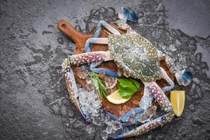 Cangrejo crudo fresco con ingredientes limón romero y lechuga para hacer comida cocida en hielo en el mercado - mariscos congelados, cangrejo azul nadando foto