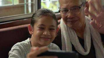 uma menina e seu avô conversando com a família por videochamada no smartphone video
