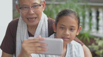 Girl and her grandfather talking with friends through video call on smartphone at home.