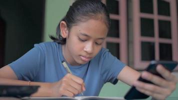 Teen girl watching her smartphone while studying at home. video