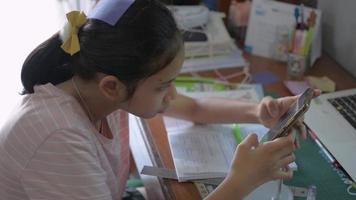 una niña estudia en línea en un teléfono inteligente en casa. video