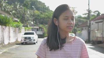 chica adolescente escuchando música desde el teléfono inteligente mientras camina por la calle. video