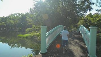 Schwenk im Park mit einer Frau in Sportkleidung, die auf einer alten Betonbrücke über einen Naturteich joggt. video