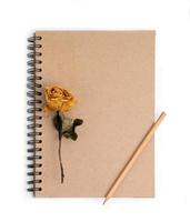 dried rose flower with pencil on notebook photo