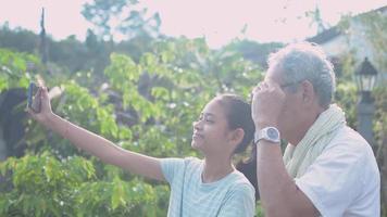 una niña y su abuelo se toman una selfie junto con un teléfono inteligente frente a la casa. video