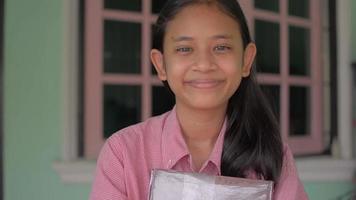 glimlachend middelbare schoolmeisje dat een boek houdt en de camera bekijkt. video