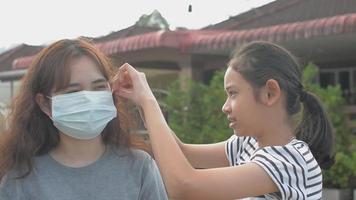 Teen girl helping her sister wearing face mask while standing outside.